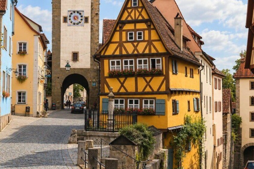 A cobblestone street with traditional half-timbered houses, a clock tower, and an archway. 3