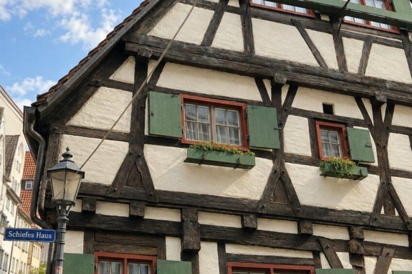 A half-timbered building with green shutters and a street sign reading 'Schiefes Haus'. 5