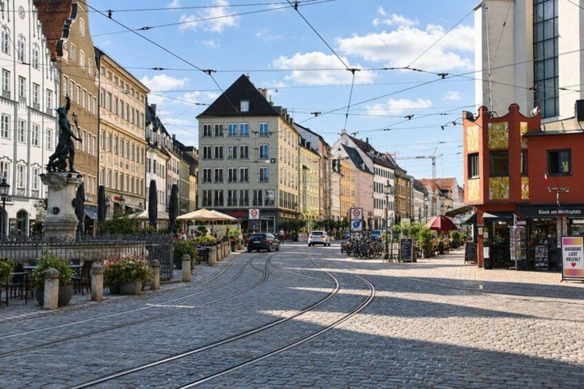 A cobblestone street with tram tracks, historic buildings, and a statue. 2