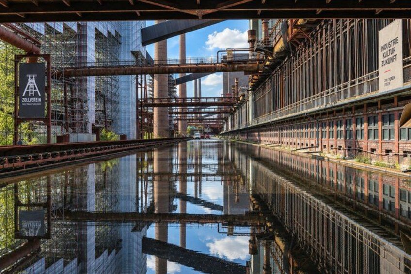 A river reflecting industrial buildings and a bridge. 3