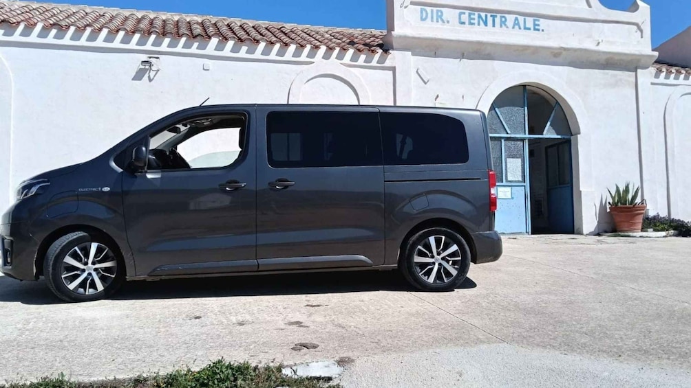 A gray van parked in front of a building with a sign that reads 'DIR. CENTRALE.' 1