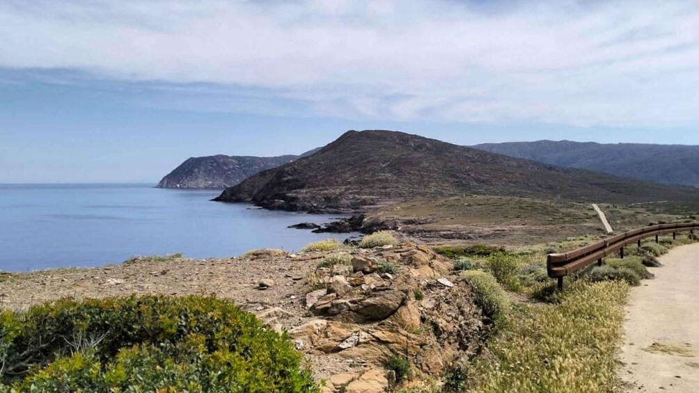 A coastal landscape with a rocky path, a wooden fence, and a mountain in the background. 3
