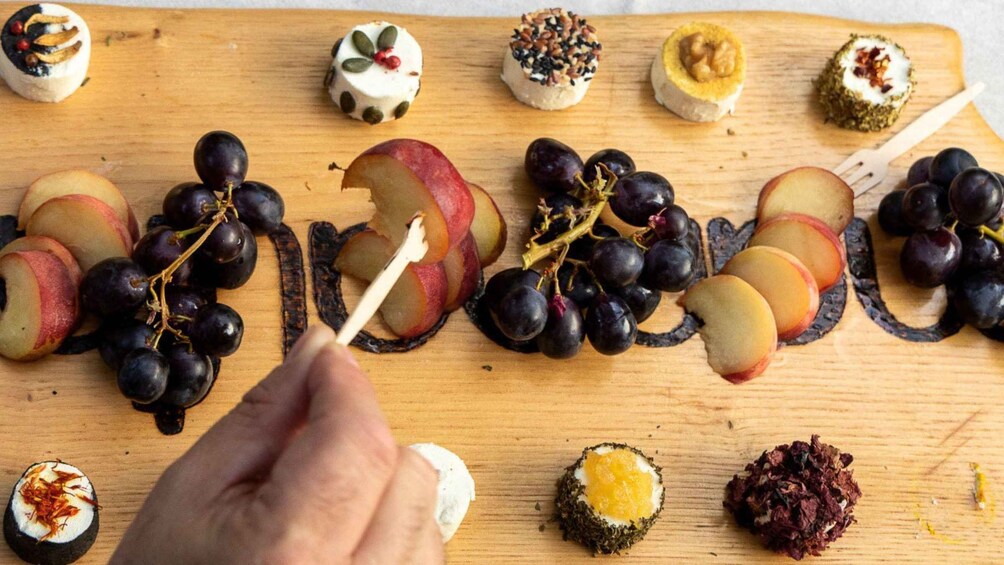 A wooden board with various food items, including grapes, apple slices, and a hand holding a toothpick. 4