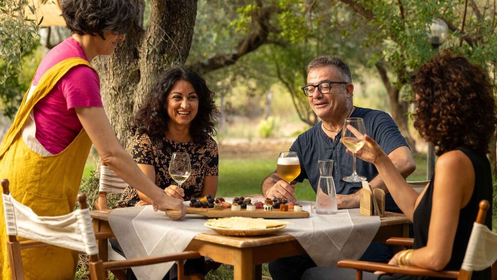 A group of people enjoying a picnic outdoors with a variety of cheeses and fruits on a table. 1