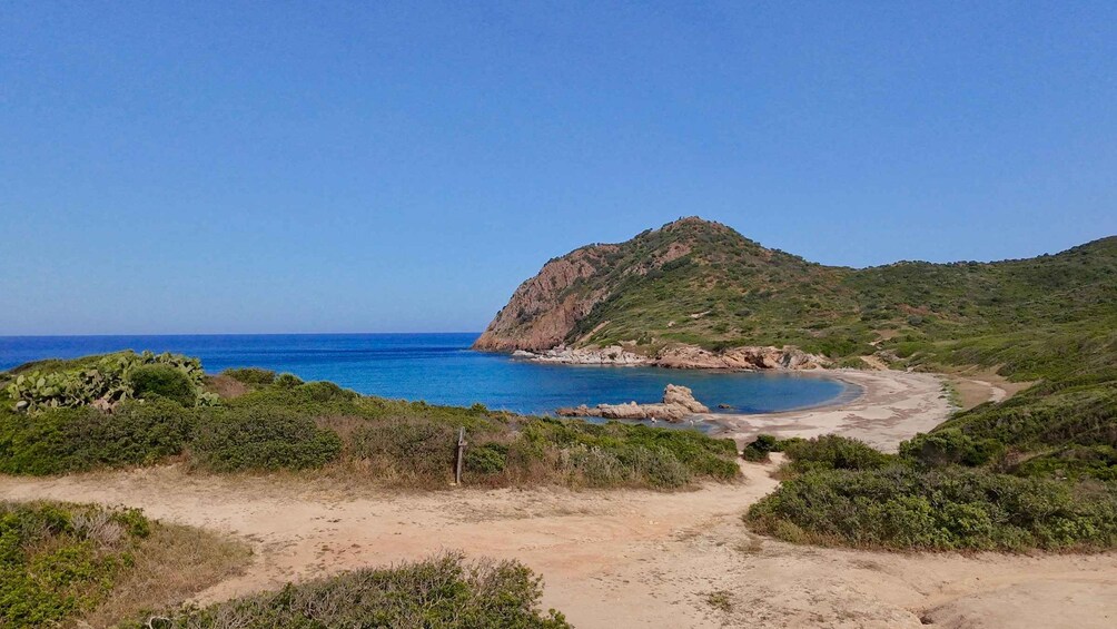 Paesaggio costiero con una spiaggia sabbiosa, un promontorio roccioso e un mare blu limpido. 5