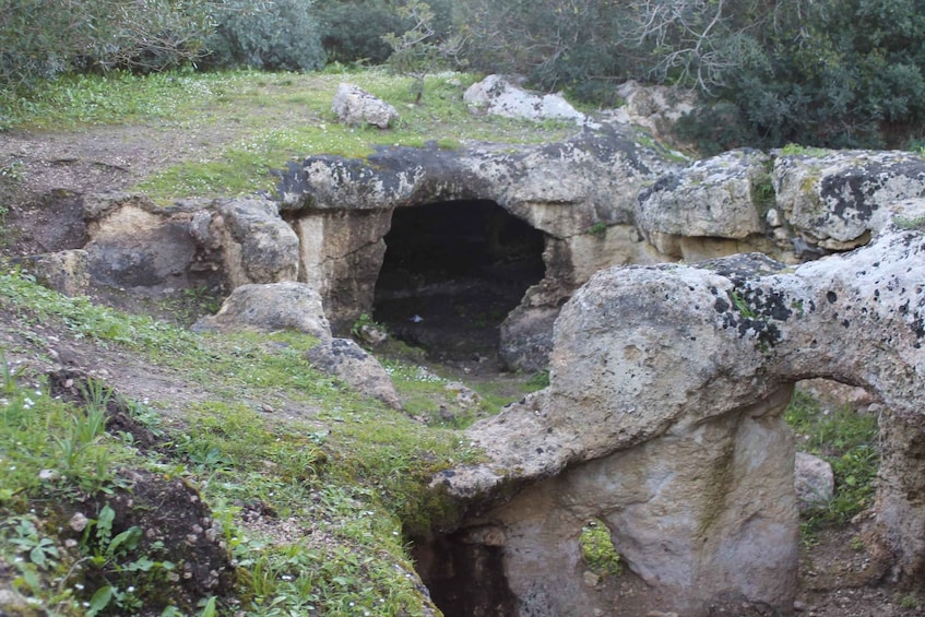 An ancient stone structure with a cave-like entrance surrounded by grass and rocks. 3