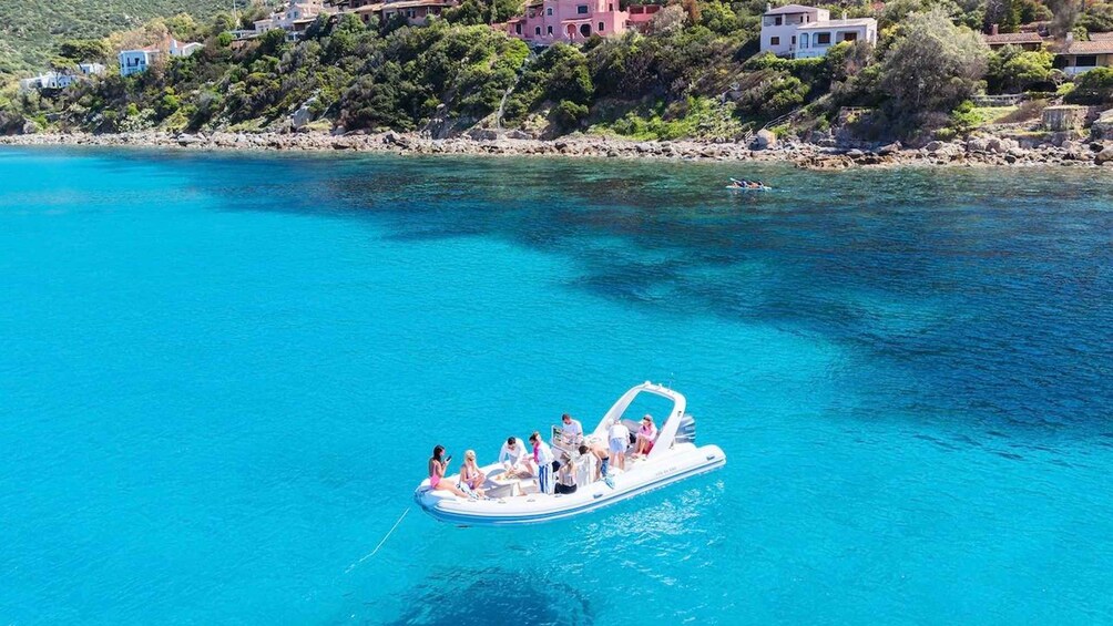 A boat with people on a clear blue sea, surrounded by rocky coastline and buildings. 4