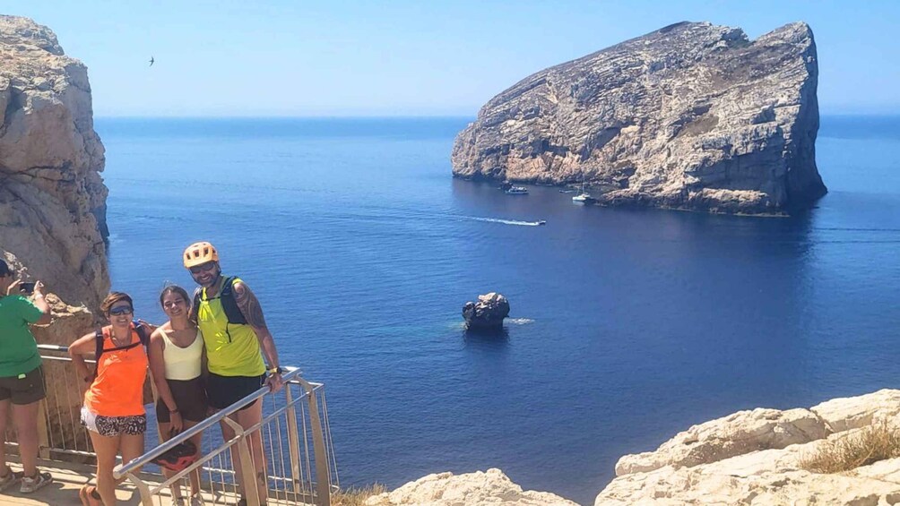 A group of people on a cliff overlooking a calm sea with a large rock formation in the distance. 3