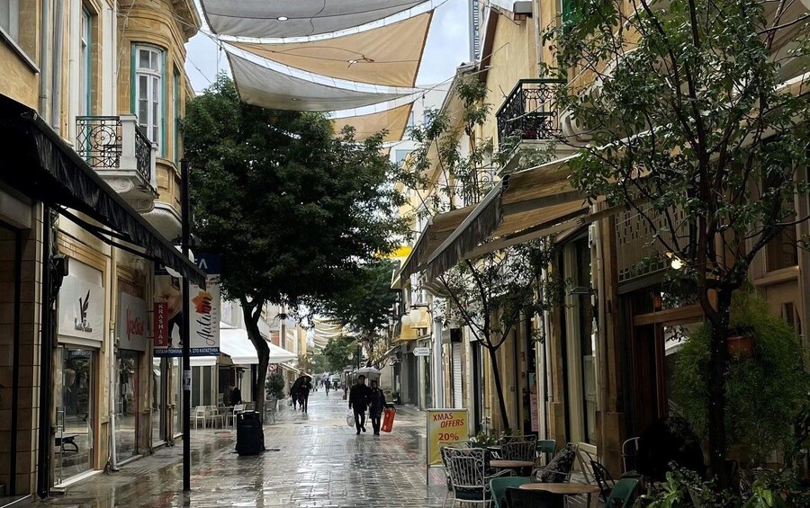 Une rue mouillée, bordée de boutiques des deux côtés, avec des arbres et des passants. 4