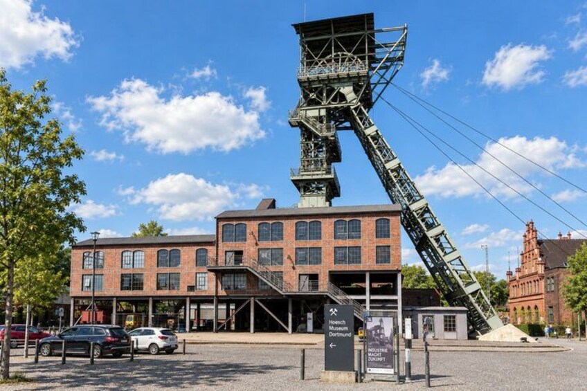A historic building with a large metal structure, a parking lot, and a red brick building in the background. 5