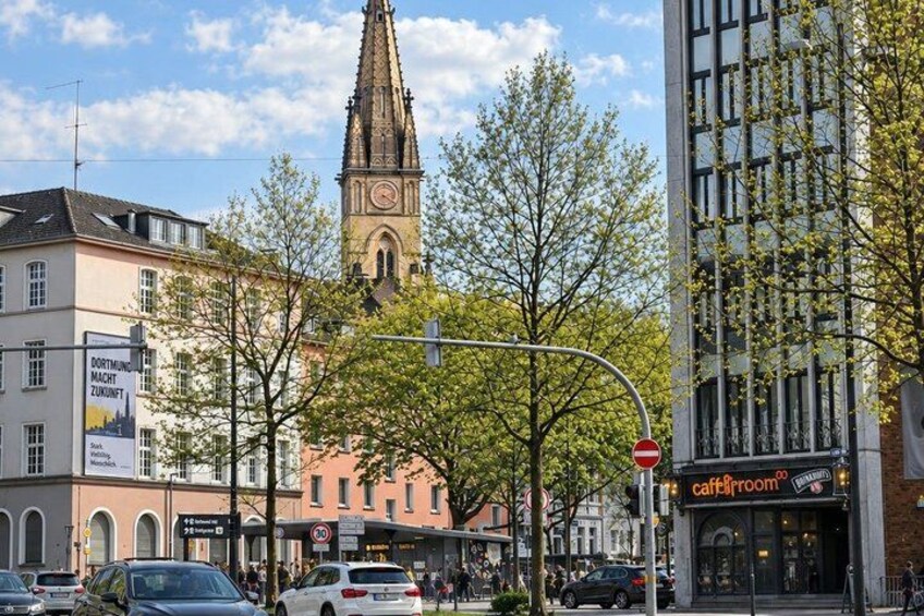 A city street with a church tower, a cafe, and various buildings. 3