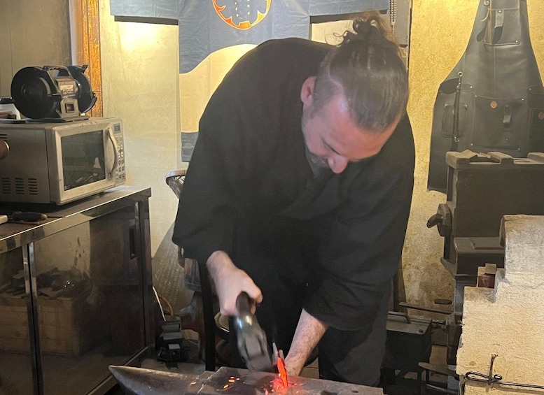 A person working with a metal object, possibly welding or forging, in a workshop with a microwave and other equipment in the background. 3