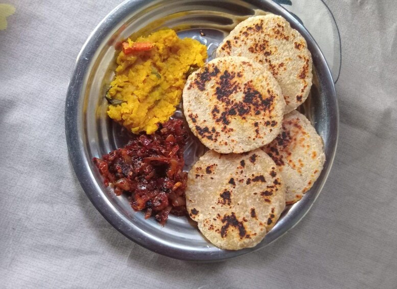 A metal plate with three pieces of flatbread, a yellow vegetable dish, and a red chutney. 2