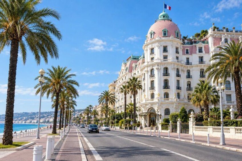 A coastal road lined with palm trees and a large building with a pink dome. 2