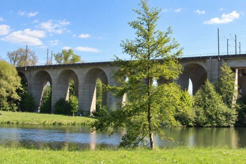 A stone bridge over a river with trees and grass in the foreground. 2