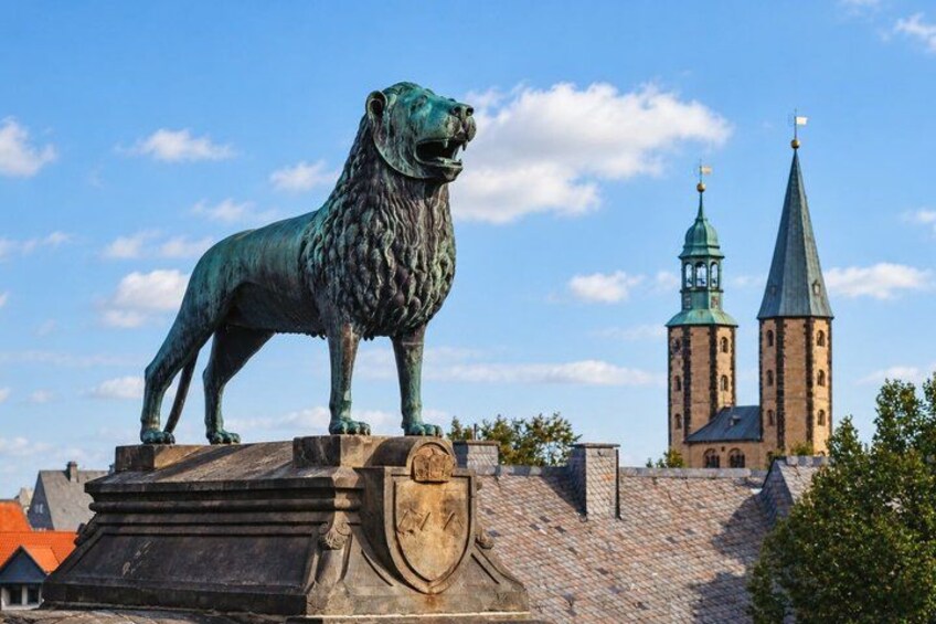 A bronze lion statue on a pedestal, a church with two towers, and a clear blue sky. 5