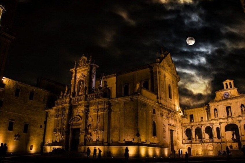 A historic cathedral with intricate architecture, a full moon in the sky, and a crowd of people in the foreground. 3