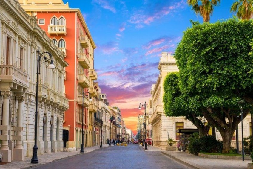 A street lined with colorful buildings, a tree-lined sidewalk, and a clear sky. 4