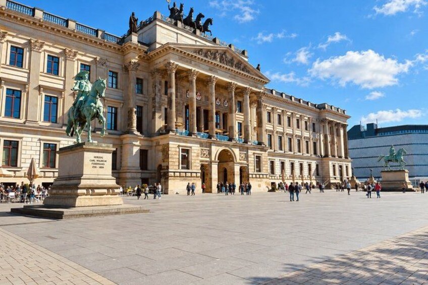 A large historic building with classical architecture, a statue of a man on a horse, and a modern structure in the background. 4
