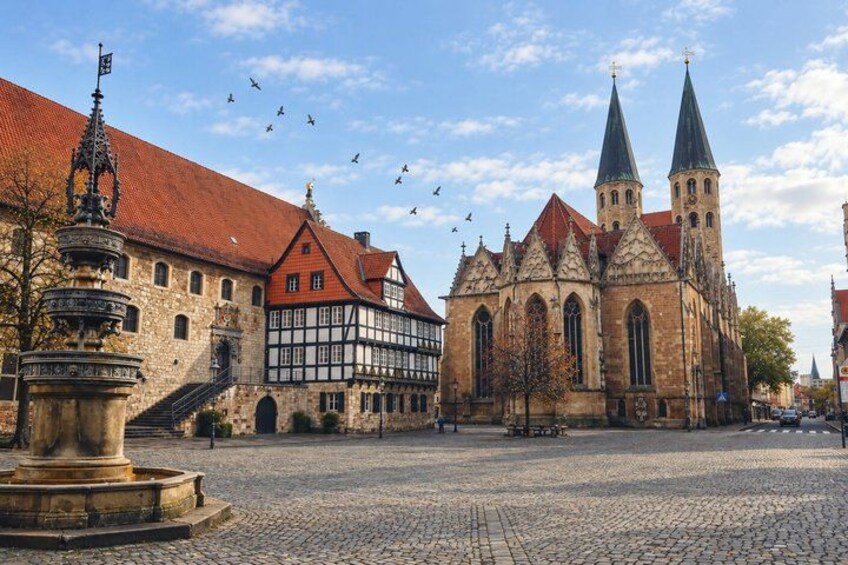 A cobblestone square with historic buildings, including a church with two spires and a half-timbered house. 2