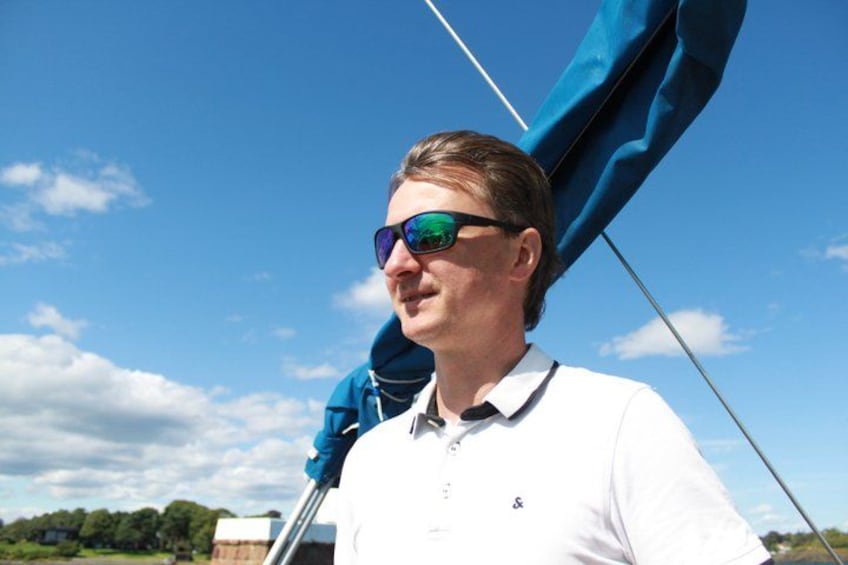 A person wearing a white polo shirt and sunglasses, standing on a boat with a blue canopy. 2