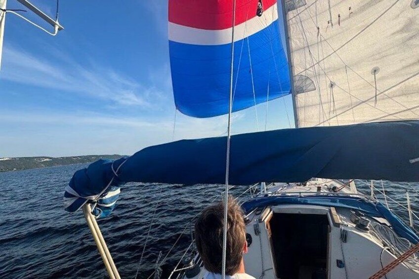 A sailboat with a blue and red sail, a person at the helm, and calm waters. 3