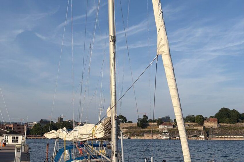 A sailboat with white sails, docked near a waterfront with buildings and trees in the background. 5