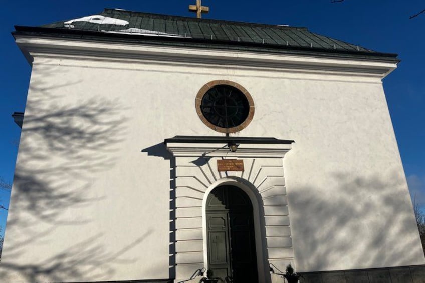 A white building with a cross on top, a circular window, and an arched entrance. 3