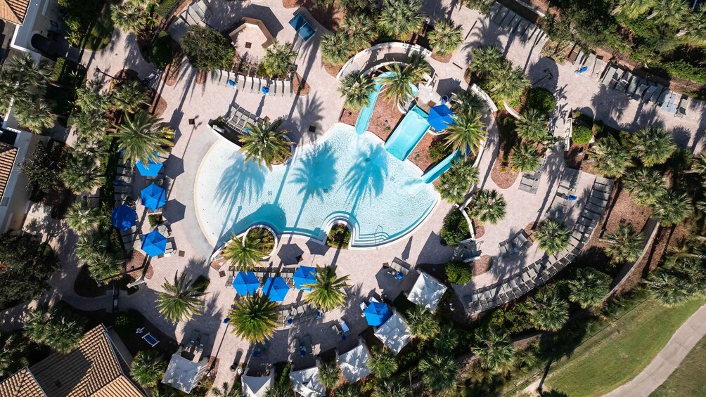 An aerial view of a resort with a large pool, palm trees, and lounge areas. 2