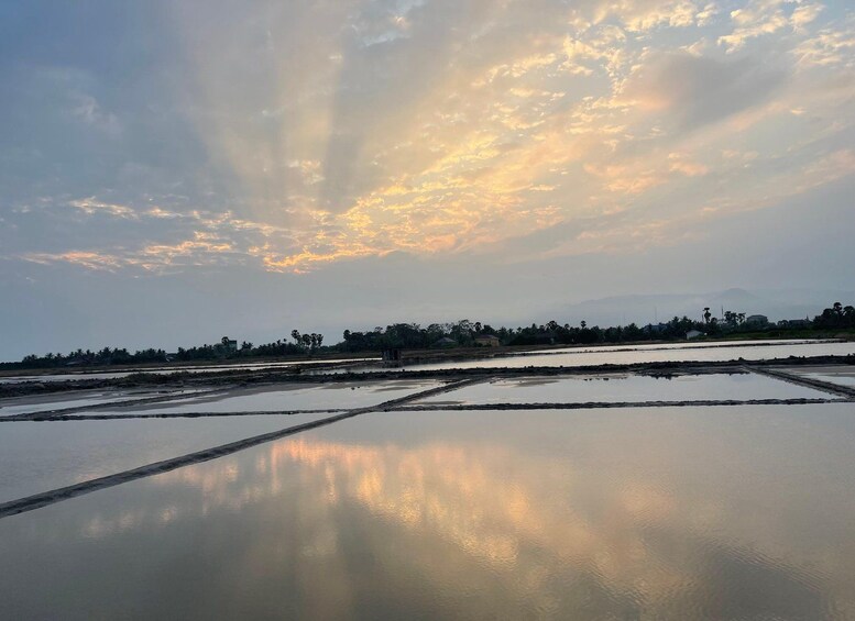 A calm water body reflecting the sky, surrounded by land with scattered trees and buildings. 1