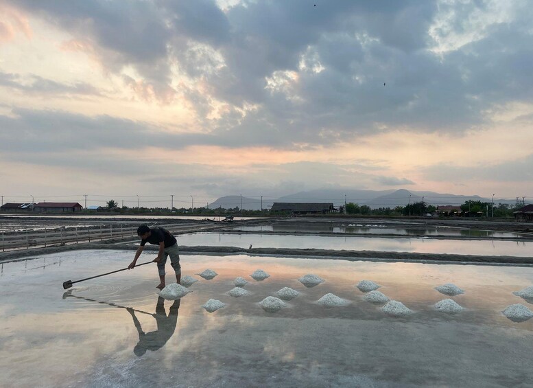 A person working in a salt flat with reflective water and scattered salt piles. 1