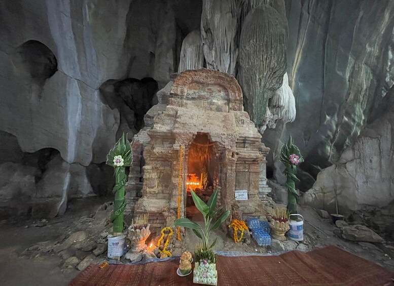 A cave shrine with a stone structure, candles, flowers, and offerings. 2