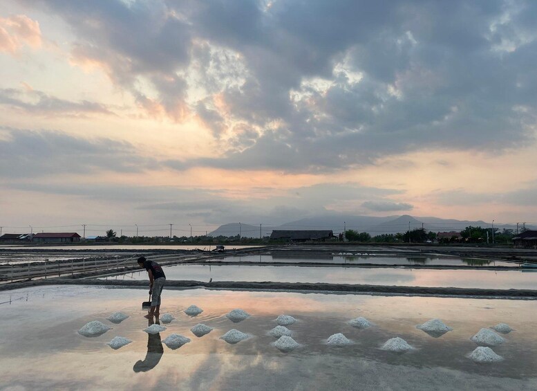 A person shoveling salt into a puddle on a reflective surface with a cloudy sky and distant mountains in the background. 5