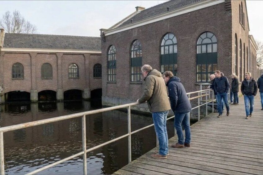 A wooden boardwalk with people walking and standing by a brick building with arched windows. 4