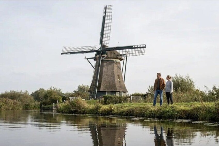 A windmill, a body of water, and two people standing near the water's edge. 5
