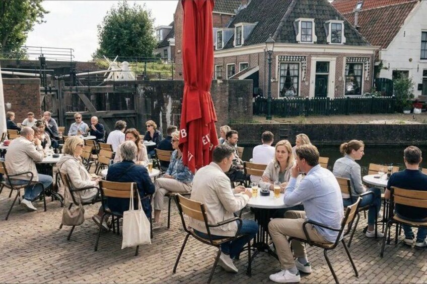 People sitting at tables outdoors, a red umbrella, and buildings in the background. 2