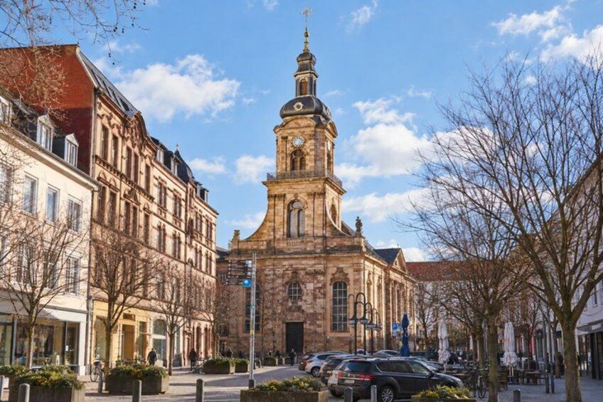 A historic church with a prominent tower, surrounded by traditional European buildings and a clear sky. 2