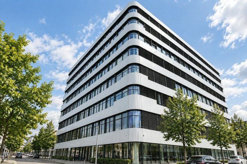 A modern multi-story building with a curved facade, surrounded by trees and a clear sky. 3