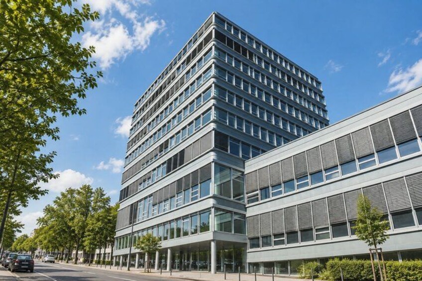 A modern multi-story building with large windows, surrounded by trees and a clear sky. 4