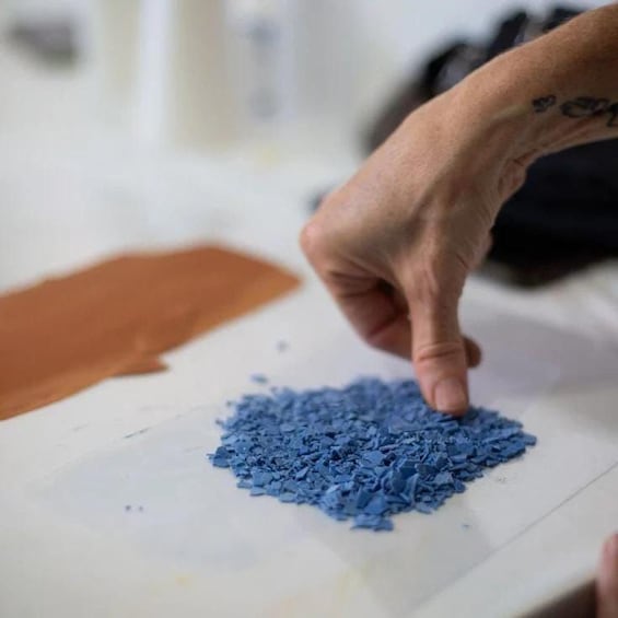 A hand touching a pile of blue powder on a white surface. 3