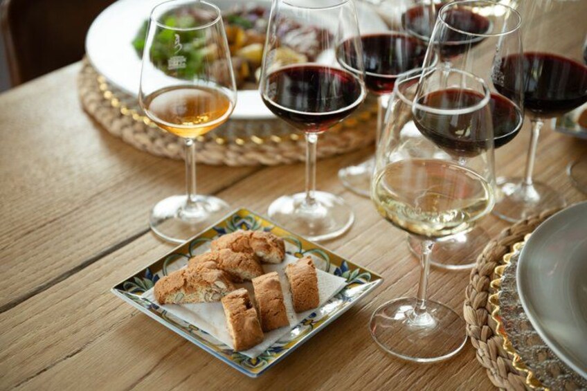 A wooden table with a plate of biscuits, several wine glasses with red and white wine, and a woven placemat. 2