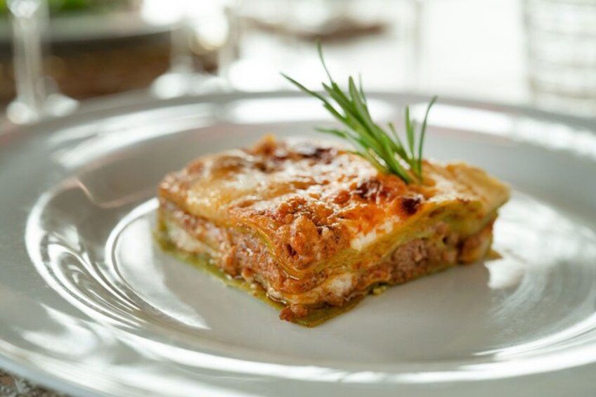 A slice of lasagna on a white plate with a sprig of rosemary on top. 3