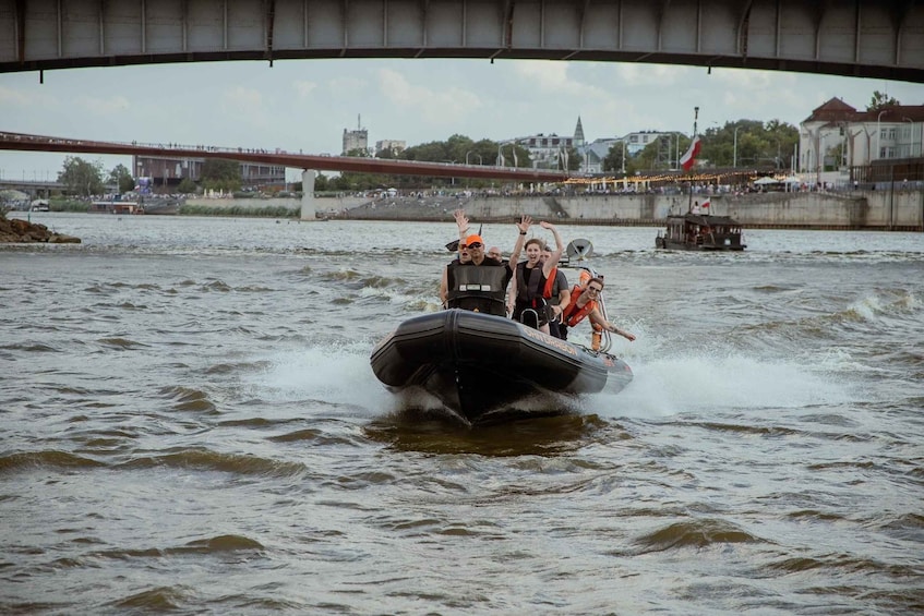 A group of people on a speedboat under a bridge, with a river and cityscape in the background. 5