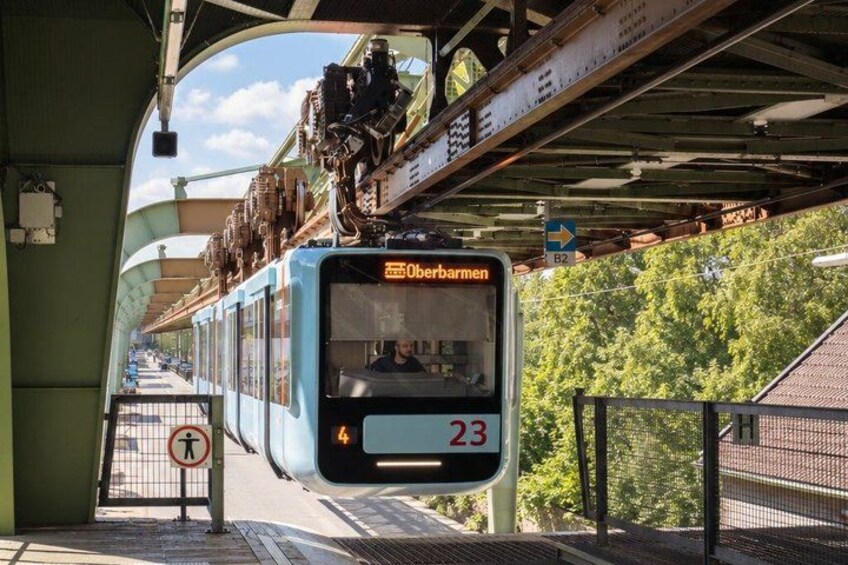 A blue bus with the destination 'Obberbarmen' and route number '23' approaching a station. 5
