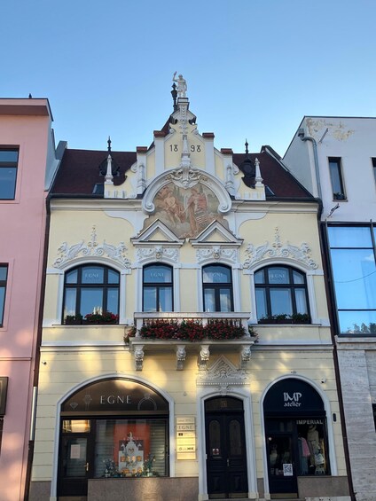 A historic building with ornate architectural details, including a central fresco, decorative windows, and a prominent entrance with the name 'EGNE'. 3