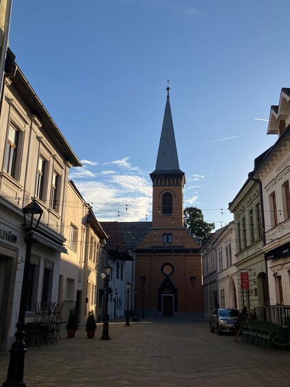 A cobblestone street with historic buildings, a church with a tall steeple, and a clear blue sky. 5