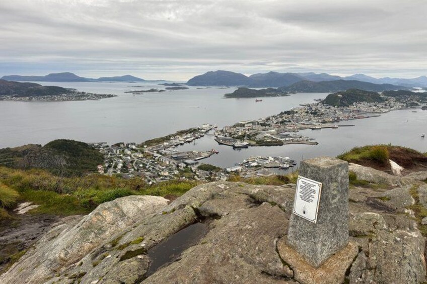 A coastal town with a rocky foreground, a signpost, and a view of the sea and distant islands. 1