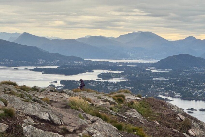 A hiker on a rocky outcrop overlooking a lake and mountains. 4