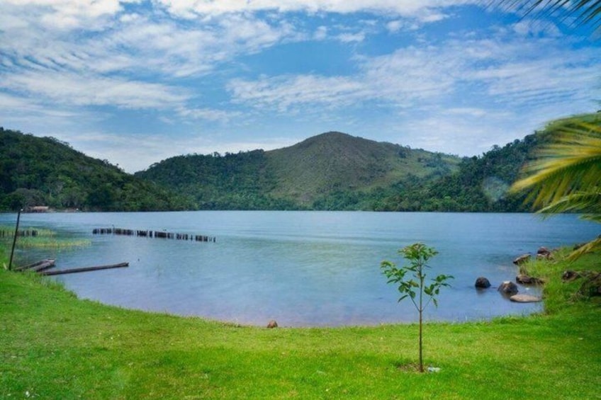 A calm lake surrounded by green hills, a small tree, and a dock. 4