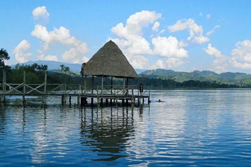 A thatched-roof hut on stilts over calm water with a mountain range in the background. 5
